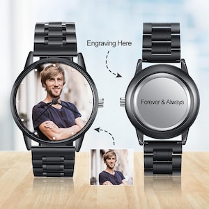 Può includere: Due orologi da polso neri. Un quadrante mostra una foto a colori di un uomo, l'altro quadrante è inciso con "Forever & Always". Gli orologi hanno cinturini in metallo nero e sono esposti su una superficie marrone chiaro.