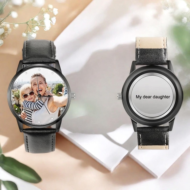 Puede incluir: Dos relojes de pulsera negros con correas de cuero. Una esfera muestra una foto de una mujer y un ni&ntilde;o, la otra tiene el texto "My dear daughter". Ambos relojes tienen cajas negras y agujas blancas.