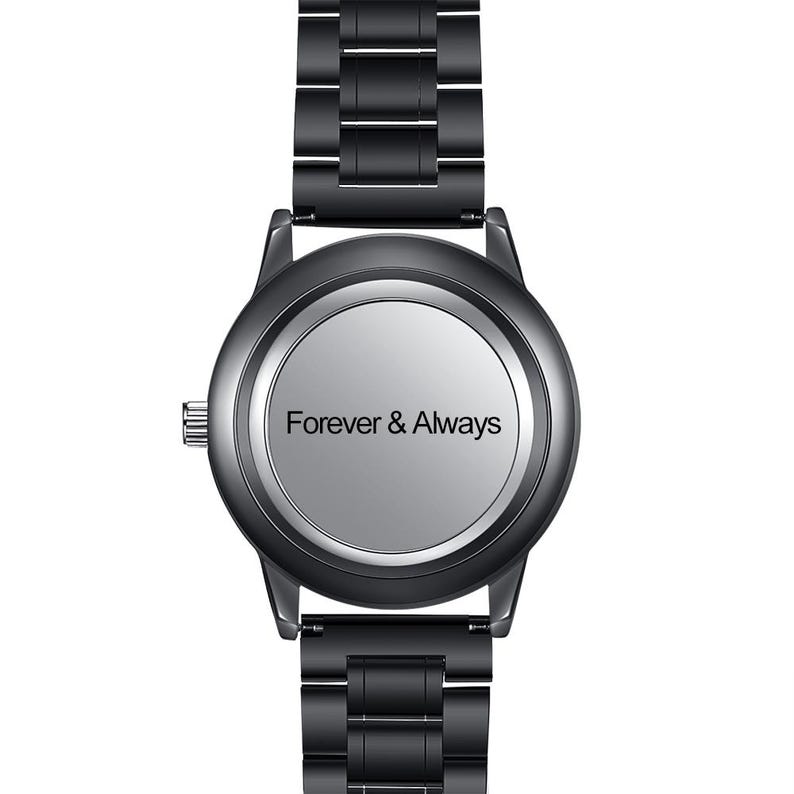 Op de afbeelding: Een zwart polshorloge met een zilveren wijzerplaat. De wijzerplaat toont de woorden "Forever & Always" in een eenvoudig lettertype. Het horloge heeft een zwarte metalen band.