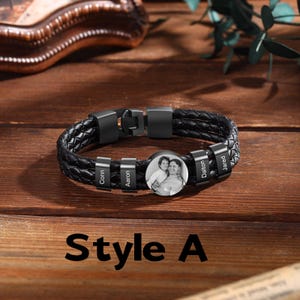 May include: Black braided leather bracelet with a metal clasp. The bracelet features a circular charm with a photo and several smaller charms with names. The text "Style A" is at the bottom.