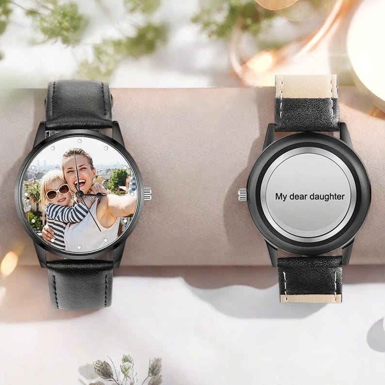 Puede incluir: Dos relojes de pulsera negros con correas de cuero. Una esfera muestra una foto de una mujer y un ni&ntilde;o, la otra tiene el texto "My dear daughter". Ambos relojes tienen cajas negras y agujas blancas.