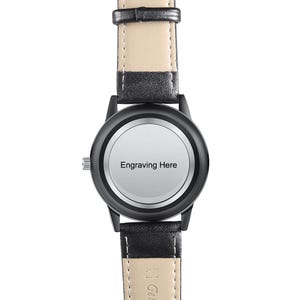 Puede incluir: Reloj de pulsera negro con bisel negro y esfera clara con la inscripci&oacute;n "Engraving Here". El reloj tiene una correa de cuero negro con la parte inferior de color claro. Dise&ntilde;o cl&aacute;sico.