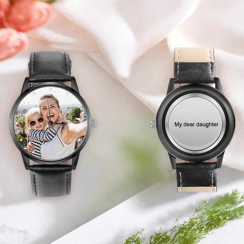 Puede incluir: Dos relojes de pulsera negros. Una esfera muestra una foto de una mujer y un ni&ntilde;o. La otra esfera es blanca con el texto "My dear daughter". Ambos relojes tienen correas de cuero negro y cajas negras.