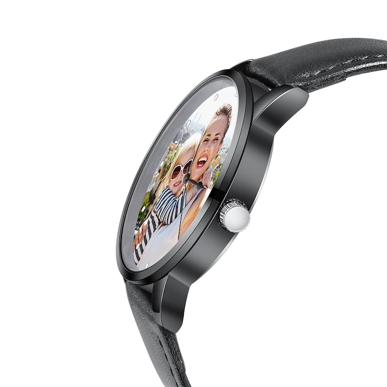 Puede incluir: Un reloj de pulsera negro con una correa de cuero gris. La esfera del reloj muestra una fotograf&iacute;a en color de dos personas. El reloj tiene un bisel negro y una corona plateada. La correa mide aproximadamente 2 cm de ancho.