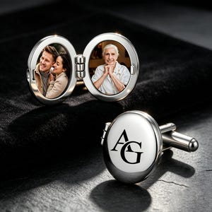 May include: A pair of silver-toned oval cufflinks. One cufflink is open, revealing two circular photo inserts: one showing a couple and the other an older person. The second cufflink is closed, displaying the black engraved letters AG on its surface.