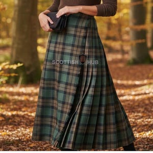 May include: A long, pleated tartan skirt in shades of green, brown, and black. The skirt features a wrap-around design and is worn with a brown top. The image is set outdoors with a blurred background of trees and fallen leaves.