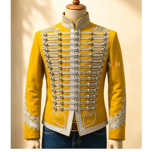 May include: A mustard yellow military-style jacket featuring a high collar, silver metallic braided trim, and rows of silver spherical buttons down the front. The sleeves and chest are decorated with intricate silver embroidery and scrollwork.
