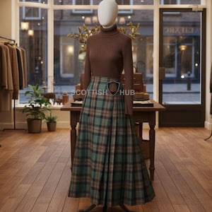 May include: A mannequin displays a brown turtleneck sweater paired with a long, pleated tartan skirt in shades of green, brown, and blue. The skirt has a classic plaid pattern. The outfit is displayed in a clothing store setting.
