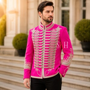 May include: A bright pink military-style jacket with silver-colored trim and decorative embroidery. The jacket features multiple rows of silver buttons and a high collar. The letters "SKH" are visible on the jacket.