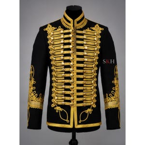 May include: A black military-style jacket featuring intricate gold braided cord detailing across the front, a high collar, and gold-toned buttons. The sleeves and chest are adorned with elaborate gold embroidery. The letters SKH appear in red and black.