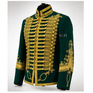 May include: A dark green military-style jacket featuring elaborate gold braided cord detailing across the front, a high collar, and gold buttons. The sleeves and front panels are decorated with intricate gold embroidery and the letters SKH.