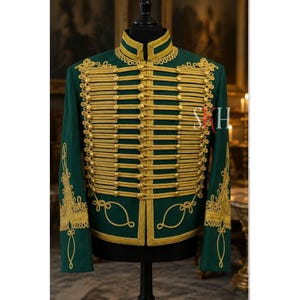 May include: A dark green military-style jacket with gold-colored trim and accents. The jacket features a high collar, multiple rows of gold braid, and decorative embroidery on the sleeves. The jacket is displayed on a black mannequin.
