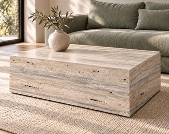 May include: A rectangular coffee table crafted from beige travertine stone with a porous, natural texture. The table features a low-profile, block-like design with visible horizontal veining and a smooth top surface holding a round vase.