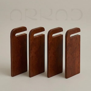 May include: Four rectangular dark brown wooden cutting boards standing upright in a row. Each board features a smooth finish, a rounded top edge, and a rectangular cutout handle near the top. The word ARKAD is visible in light grey text above.