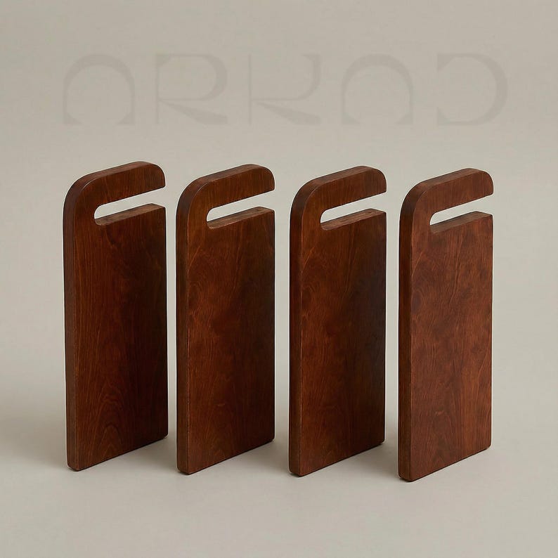 May include: Four rectangular dark brown wooden cutting boards standing upright in a row. Each board features a smooth finish, a rounded top edge, and a rectangular cutout handle near the top. The word ARKAD is visible in light grey text above.