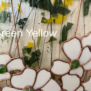 May include: A stained glass panel featuring white flower shapes outlined in copper foil, accented with small green glass centers. The background consists of clear glass with scattered green and yellow glass shards and black wire lines. Text reads Green Yellow.