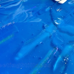 May include: A vibrant blue liquid surface with a glossy, reflective texture. The number 249 is printed in white in the upper left corner, and the text FleetingStillness is printed in white along the bottom edge of the frame.