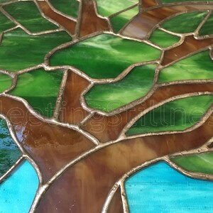 May include: Close-up of a stained glass tree with green and brown glass pieces. The glass is set in a silver metal frame.