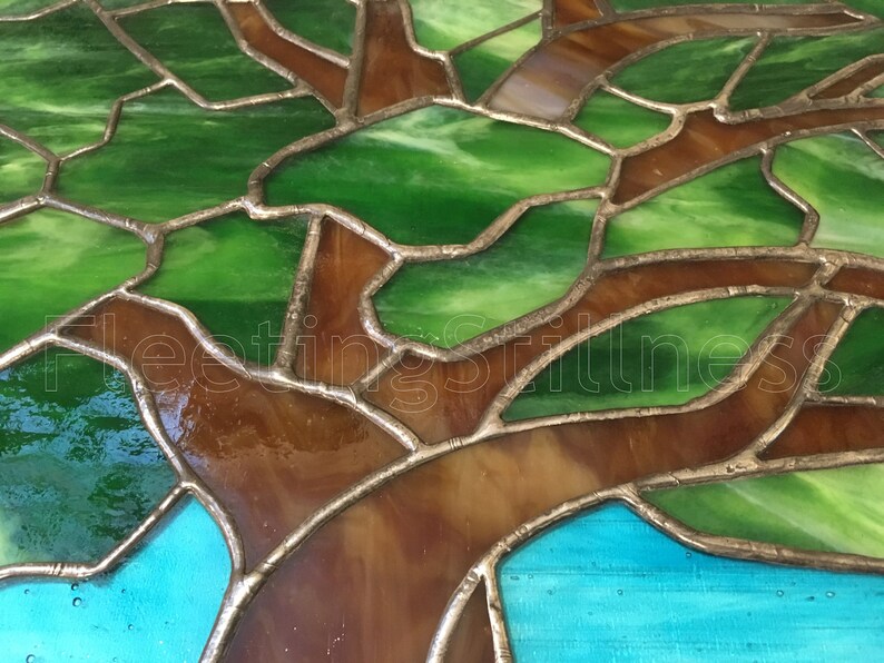 May include: Close-up of a stained glass tree with green and brown glass pieces. The glass is set in a silver metal frame.