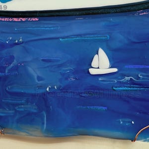 May include: A rectangular fused glass art piece featuring a deep blue ocean scene with a small white sailboat. The glass has a smooth, glossy finish with subtle horizontal textures. The number 249 is printed in the top left corner.