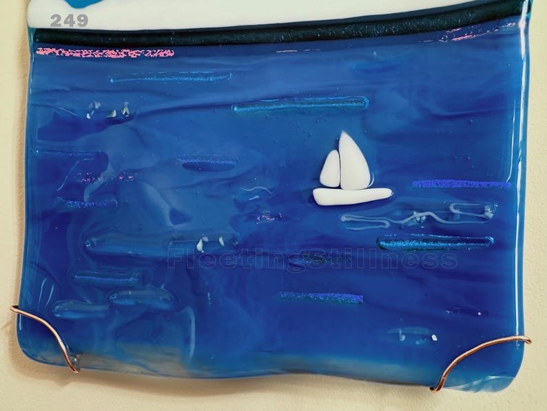 May include: A rectangular fused glass art piece featuring a deep blue ocean scene with a small white sailboat. The glass has a smooth, glossy finish with subtle horizontal textures. The number 249 is printed in the top left corner.