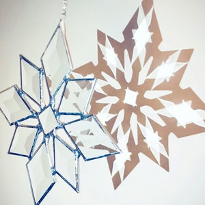 May include: A silver glass snowflake ornament hangs from a string, casting a shadow of a white snowflake on a white wall.