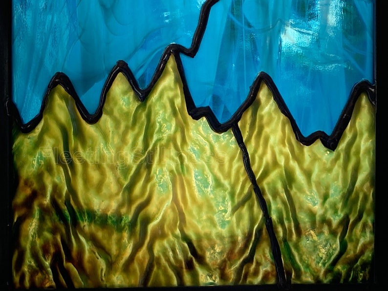 May include: A stained glass window panel depicting a mountain range with a blue sky above. The mountains are outlined in black and have a textured, green surface.