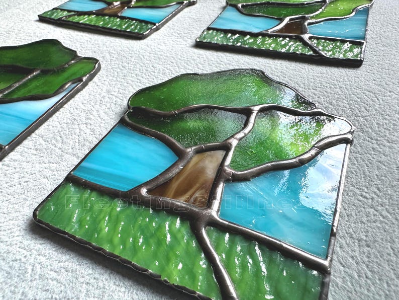 May include: A set of square stained glass panels featuring a tree design with a brown trunk, green foliage, and a bright blue sky background. Each panel is constructed with dark metal solder lines separating the individual glass pieces.