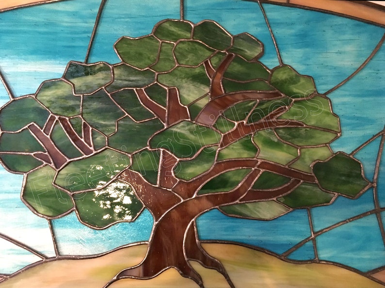 May include: A stained glass window depicting a tree with green leaves and a brown trunk against a blue sky background.