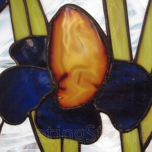 May include: A stained glass window featuring a stylized iris flower with blue and yellow petals. The center of the flower is made of a brown and orange agate stone.