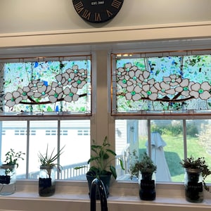 May include: Two rectangular stained glass window panels featuring white dogwood flowers with green glass centers on brown branches, set against a background of clear, blue, and green textured glass pieces held together by copper foil solder lines.