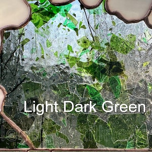 May include: A stained glass panel featuring a mosaic of light and dark green glass shards encased in copper foil solder lines, with opaque cream-colored glass borders. The text Light Dark Green is printed in white across the center.