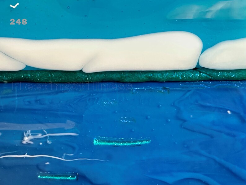 May include: A layered abstract artwork featuring a bright blue sky, a horizontal band of white clouds, a dark green textured strip, and a deep blue water surface with subtle light blue ripples and the text 248 and Fleetingstillness.