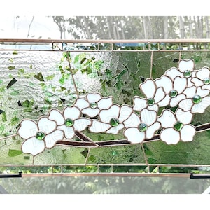 May include: A rectangular stained glass panel featuring white dogwood flowers with green glass centers on a brown branch. The background consists of textured clear and green glass pieces framed in copper metal with a grid border design.