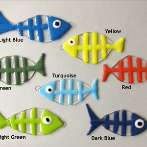 K&ouml;nnte beinhalten: Sieben gl&auml;serne Fisch-Ornamente mit einem Skelett-Design. Die Fische sind in den Farben hellblau, dunkelgr&uuml;n, t&uuml;rkis, rot, hellgr&uuml;n und dunkelblau. Die Fische sind alle nach rechts im Bild ausgerichtet.