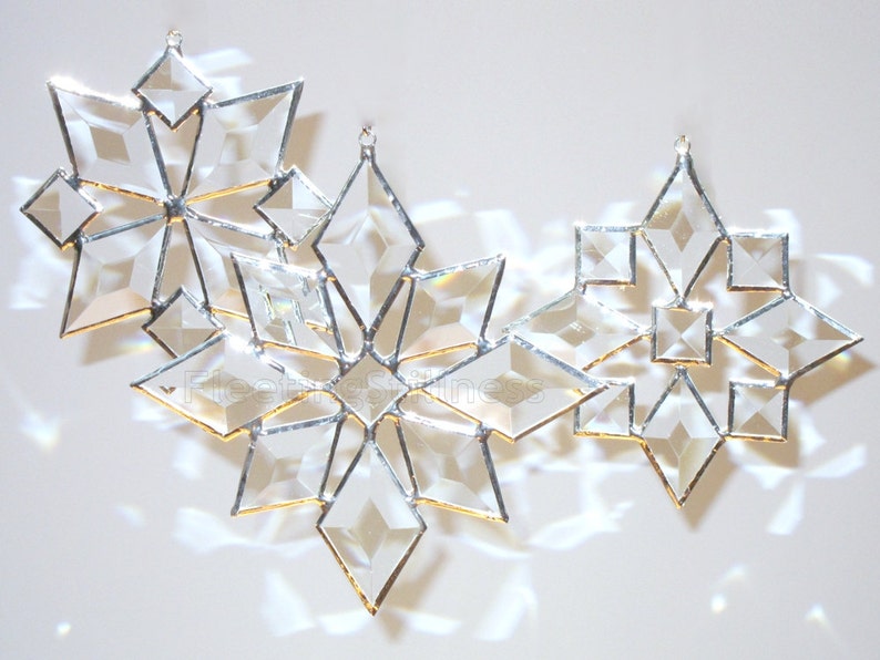 May include: Three glass snowflake ornaments with a silver finish and gold accents. The snowflakes are arranged in a row, with the largest snowflake in the center.