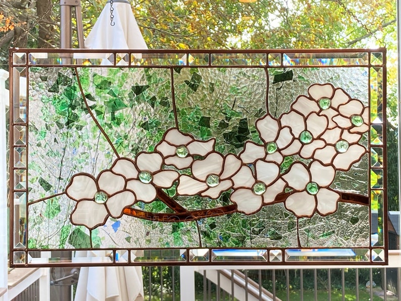 May include: A stained glass window depicting a branch of white dogwood blossoms with green leaves. The flowers are made of white and iridescent glass, with green glass for the leaves and centers of the flowers.