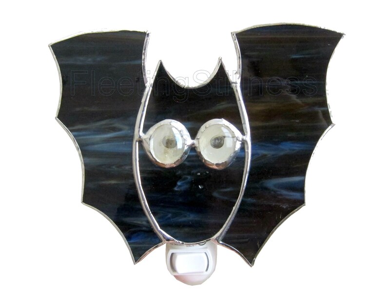 May include: A stained glass bat nightlight with a black and blue glass body and white eyes. The nightlight has a standard plug-in socket.