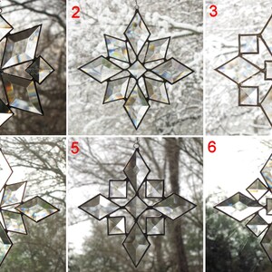 May include: Six clear glass snowflake ornaments with a geometric design. Each snowflake is suspended from a silver string and is hanging in front of a window.