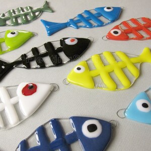 K&ouml;nnte beinhalten: Eine Sammlung von neun Glasfisch-Ornamenten mit bunten Skeletten und wei&szlig;en Augen. Die Fische sind in verschiedenen Farben, darunter Gr&uuml;n, Rot, Blau, Gelb, Schwarz und Wei&szlig;.