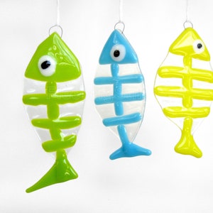 K&ouml;nnte beinhalten: Drei gl&auml;serne Fisch-Ornamente mit Skelett-Design. Die Fische sind gr&uuml;n, blau und gelb.