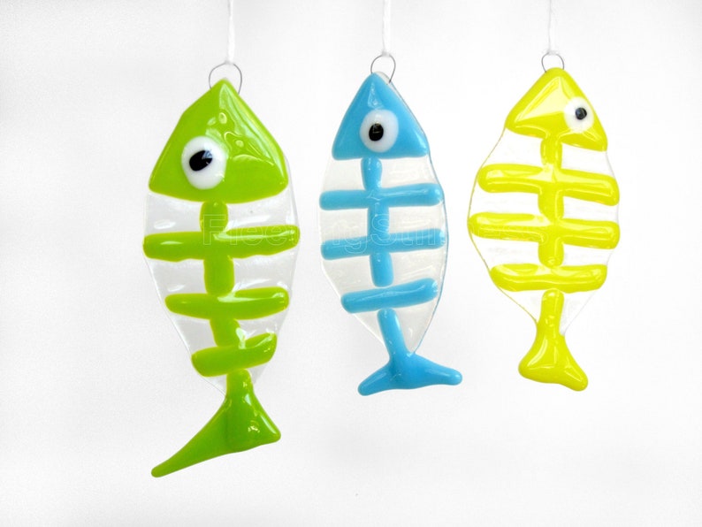 K&ouml;nnte beinhalten: Drei gl&auml;serne Fisch-Ornamente mit Skelett-Design. Die Fische sind gr&uuml;n, blau und gelb.