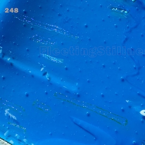 May include: A vibrant blue translucent surface featuring a scattered pattern of small raised dots and subtle linear indentations. The number 248 is printed in the upper left corner, and the text FleetingStillness appears in the center.