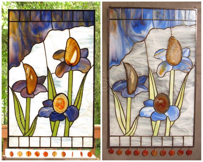 May include: A stained glass window depicting three blue iris flowers with agate accents. The flowers are set against a white background with a blue and white swirled glass sky.