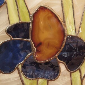 May include: A stained glass window panel featuring a stylized flower with blue, yellow, and orange glass pieces. The flower is set against a white background.