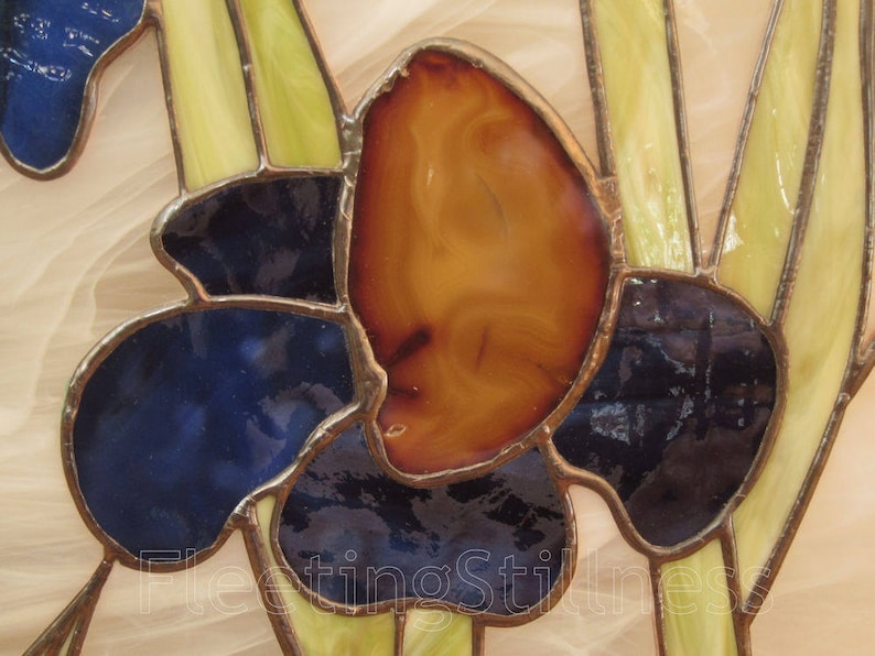 May include: A stained glass window panel featuring a stylized flower with blue, yellow, and orange glass pieces. The flower is set against a white background.