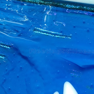 May include: A vibrant blue surface with a glossy, textured finish featuring embedded horizontal glitter strips. The number 248 is printed in the top left corner, and the text FleetingStillness is visible in the center of the blue field.