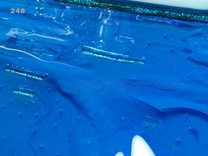May include: A vibrant blue surface with a glossy, textured finish featuring embedded horizontal glitter strips. The number 248 is printed in the top left corner, and the text FleetingStillness is visible in the center of the blue field.