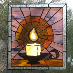 K&ouml;nnte beinhalten: Buntglasfenster mit einer Kerze in einem Halter. Die Kerze hat eine leuchtend gelbe Flamme und sitzt auf einem schwarzen Halter. Der Hintergrund ist ein radiales Design in Orange-, Gold- und Lilat&ouml;nen, umrahmt von einem schwarzen Rahmen.