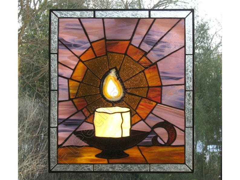 K&ouml;nnte beinhalten: Buntglasfenster mit einer Kerze in einem Halter. Die Kerze hat eine leuchtend gelbe Flamme und sitzt auf einem schwarzen Halter. Der Hintergrund ist ein radiales Design in Orange-, Gold- und Lilat&ouml;nen, umrahmt von einem schwarzen Rahmen.